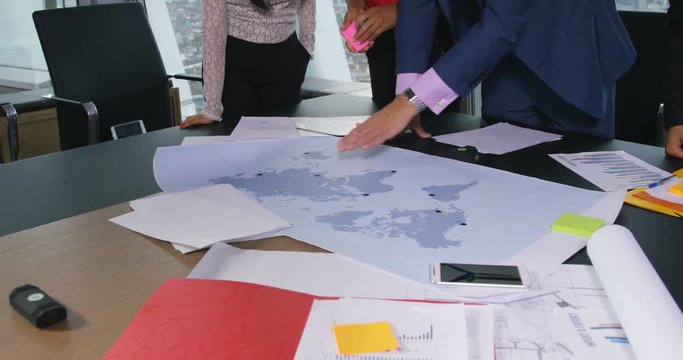 4K International business team in a meeting looking at world map & planning company growth. Slow motion.