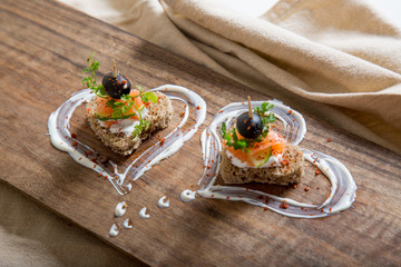 Fototapeta na wymiar Appetizer canape with salmon fish, cheese and olive on a small loaf of bread, closeup