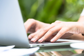 Asian woman hands has touching and typing on laptop computer with blurred coffee, computer and view outside window.