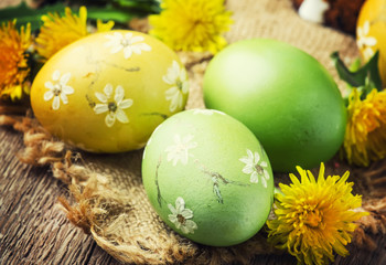 Fototapeta na wymiar Easter yellow and green eggs with spring dandelions, festive composition in rustic style, vintage wooden background, selective focus