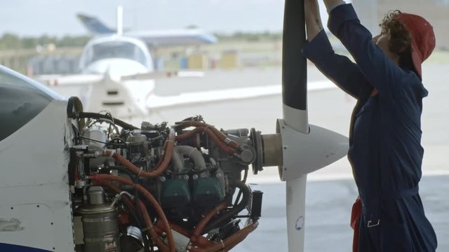 Female aircraft maintenance turning propeller of light jet airplane with exposed engine while working in hangar
