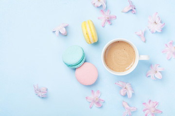 Cake macaron or macaroon, pink flowers and coffee on blue pastel background top view. Creative and fashion composition. Flat lay style.