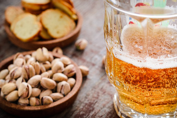 a glass of light beer, pistachios and toasts in backlight on a wooden table