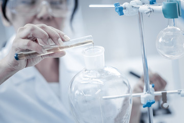 It is all about proportions. Scaled up look on a female chemist holding a test tube and pouring liquid into a separating funnel fixed on a stand while conducting a chemical experiment.