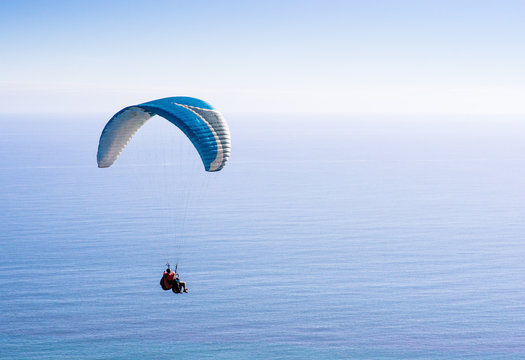 A paraglider flying over the calm blue ocean