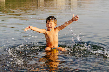 little boy splashes water. Swimming in warm lake on Sunny summer day