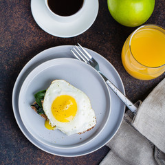 Rye bread toasts with fried spinach and egg with cup of coffee and orange juice on blue table background. Healthy Breakfast Food Concept. Top view with Copy Space