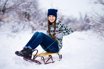 Fototapeta na wymiar Cheerful young woman having fun on a sleigh in snowy weather