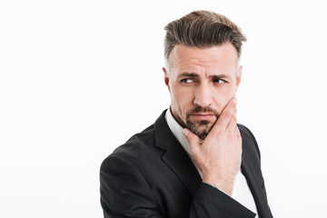 Photo of attractive businessman in suit looking aside with brooding look and touching his chin, isolated over white background