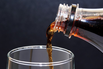 closeup on cola being poured into glass against dark background