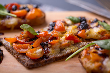 close up of delicious bruschetta with mozzarella, tomatoes and dark jam on a wooden plate