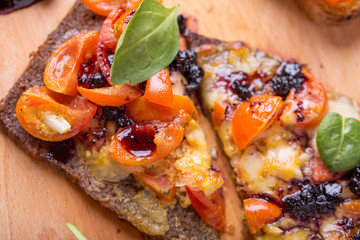 close up of delicious bruschetta with mozzarella, tomatoes and dark jam on a wooden plate