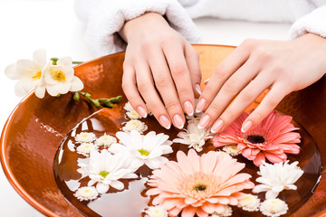 Obraz na płótnie Canvas cropped view of woman making spa procedure with flowers in beauty salon, nail care concept