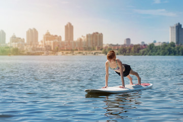 Young beautiful woman meditating on a river at SUP paddleboarding