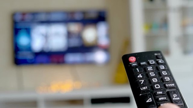 Hand hold TV remote control. TV on the background.
