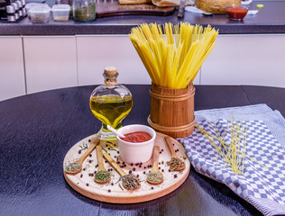 Uncooked spaghetti in wooden pot and spices on wooden plate