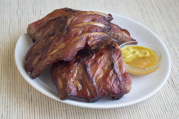 Smoked roasted pork ribs  and sauce of honey with ginger and mustard in a white dish.