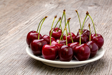Ripe cherries on a white plate on a wooden table