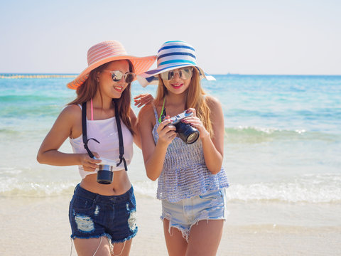 summer holiday,vacation,travel and people concept of smiling young women check a photo on beach over sea and blue sky background.Portrait of three young female friends walking on the sea shore looking