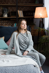 Obraz premium beautiful young woman sitting on bed in morning and looking away