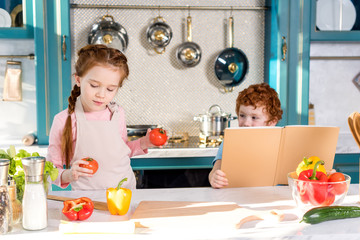 children with cookbook and vegetables cooking together in kitchen