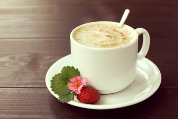 fragrant cappuccino for gourmets/ frothy coffee with whipped milk in cup is decorated with real berries of fresh strawberries with flower and leaf