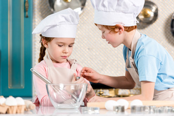 beautiful little children in chef hats and aprons cooking together in kitchen