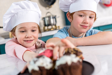 smiling little children in chef hats looking at delicious cupcakes on foreground