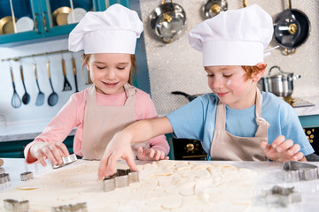 adorable little kids in chef hats and aprons preparing cookies together