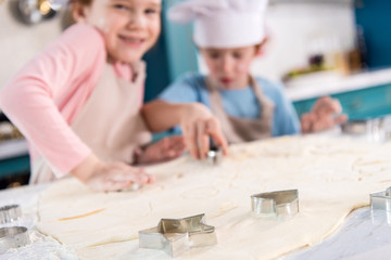 close-up view of uncooked dough and forms for cookies and cute little children in kitchen