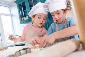 cute little children in chef hats and aprons preparing cookies together