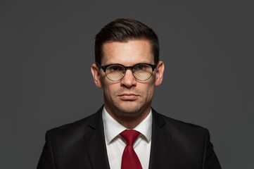 An angry businessman in formal suit and glasses looks at the camera on gray background