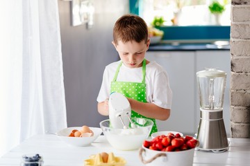 Happy child boy mixing dough in glass bowl