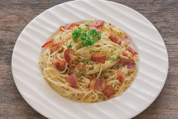 Spaghetti carbonara with bacon and cheese on white plate sprinkle with chopped parsley on wood table with copy space. Italian traditional homemade food for lunch or dinner so creamy and delicious.