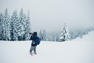 Man tourist photographer with backpack, at mountain with pine trees covered by snow. Beautiful winter landscapes. Frost nature.