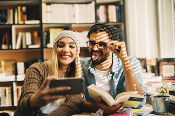 Two joyful happy smart high school students having fun while taking a selfie on a break from studying in the library.