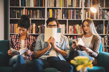 Three attractive hardworking young university students reading books in the library while a guy in...