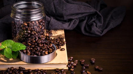 Dark coffee shop scene with coffee beans and fresh mint on wooden table. table