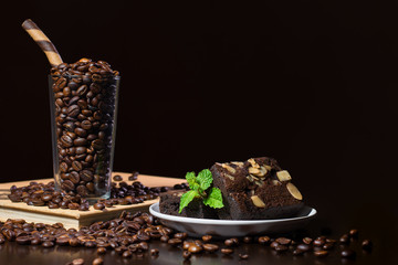 Glass of coffee beans and chocolate brownie, dark table top scene with copy space.