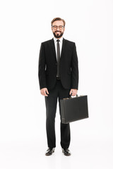 Full-length image of good-looking man in business suit posing with black briefcase and looking on camera, isolated over white background