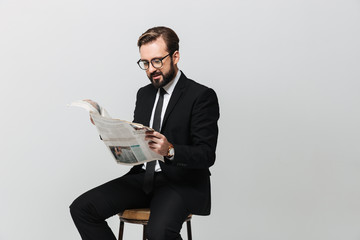 Portrait of businesslike man in office wearing suit and eyeglasses reading newspaper while sitting...
