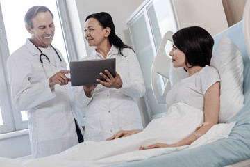 Promising result. Low angle shot of a team of doctors looking satisfied while looking at the result of a lab testing and talking to a female patient.