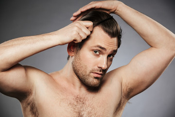 Portrait of a charming shirtless man combing his hair