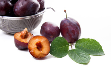 Steel colander with ripe plums, whole and half ripe plums with leaf isolated on a white background..