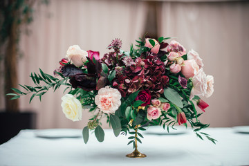 Rich bouquet of red, pink and white roses and greenery stands on the table in a luxury restaurant