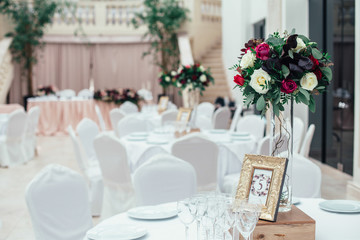 Rich bouquet of red, pink and white roses and greenery stands on the table number five in a luxury restaurant