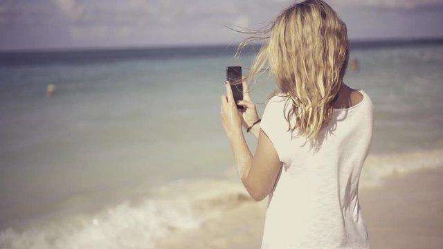 young, beautiful woman using her phone at the beach and taking pictures