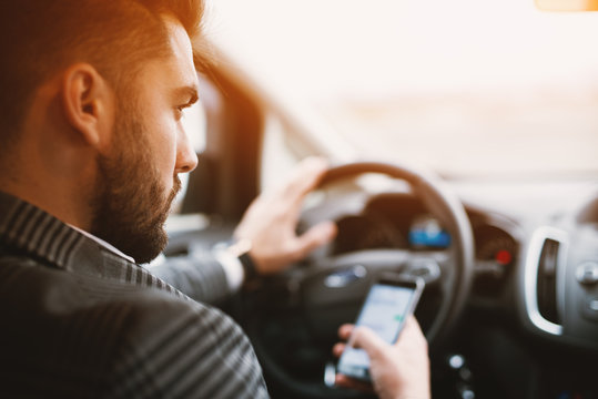 Attractive bearded man texting while driving an expencive car in a sunny weather.