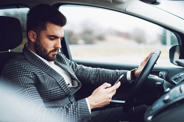 Good looking bearded businessman wearing a suit looking upset after texting while driving a car.