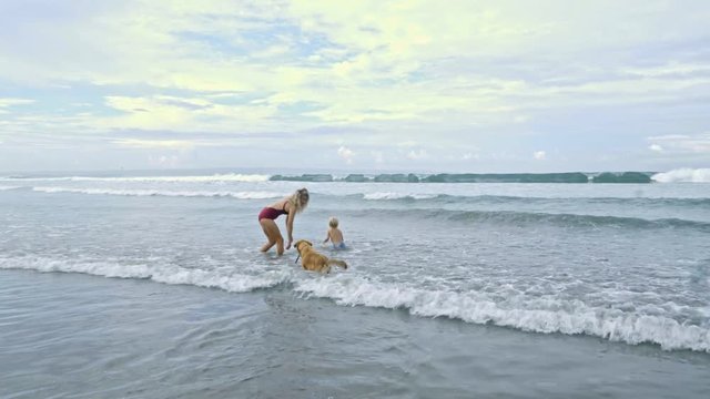 Blonde woman playing with little son and golden retriever in ocean at summer vacation